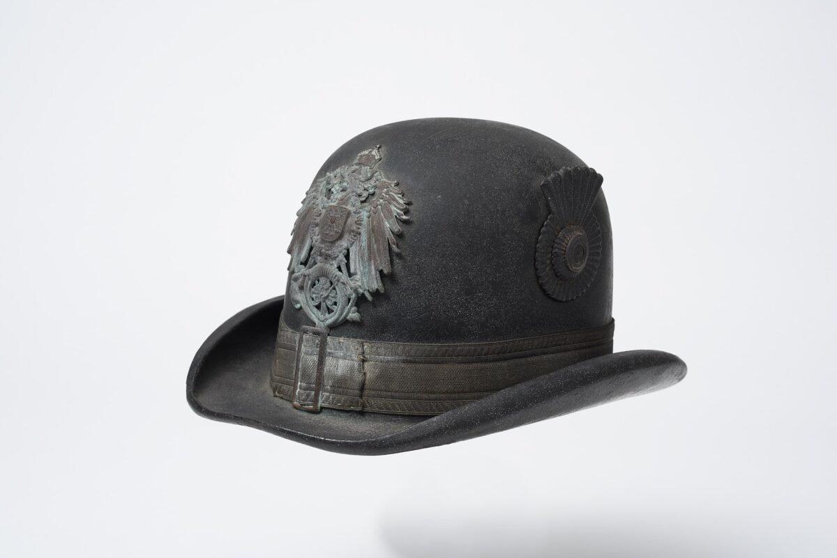 Ende des 19. Jahrhunderts, Herkunft unbekannt, Lederkorpus mit Krempe, Tressenband mit Schnalle, Reichsadler mit dem Posthorn (Emblem der Deutschen Reichspost [1871– 1919]), farbig lackierte Landeskokarde, innen: Schweißleder, Filz (Regenschutz), Sammlung: museum oder-spree (Foto: Bernd Choritz)