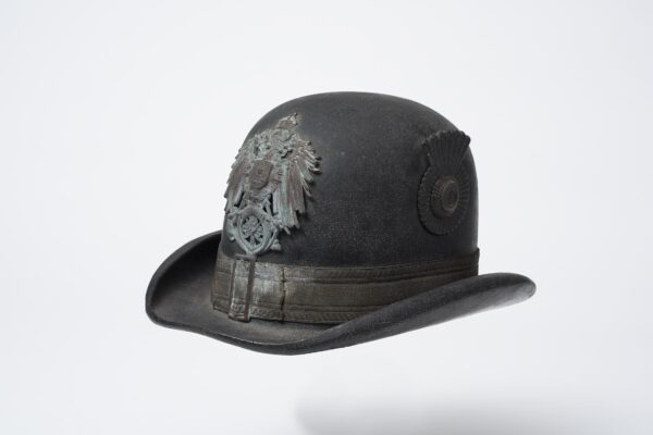 Ende des 19. Jahrhunderts, Herkunft unbekannt, Lederkorpus mit Krempe, Tressenband mit Schnalle, Reichsadler mit dem Posthorn (Emblem der Deutschen Reichspost [1871– 1919]), farbig lackierte Landeskokarde, innen: Schweißleder, Filz (Regenschutz), Sammlung: museum oder-spree (Foto: Bernd Choritz)